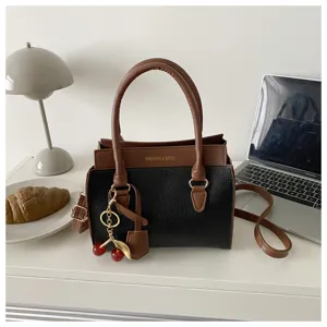 Chic colorblock handbag detail view showcasing elegant brown and black leather with cute cherry charm.