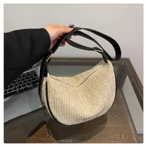 Détail en gros plan du sac bandoulière en paille tissée avec une lanière en cuir noir.