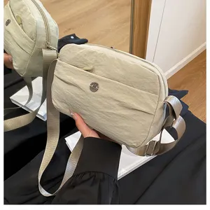Detailed view of the beige crinkled fabric crossbody bag with metal badge and strap.