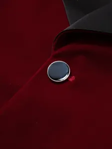 Men's velvet suit jacket detail close-up showing burgundy fabric, black lapel and button.