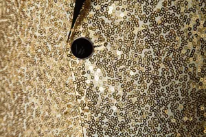 Close-up of men's shiny gold sequin suit jacket detail showing sequins and black button.