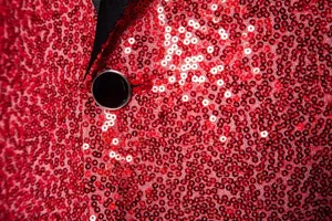 Close-up detail of men's sparkling red sequin blazer jacket with black lapel button.