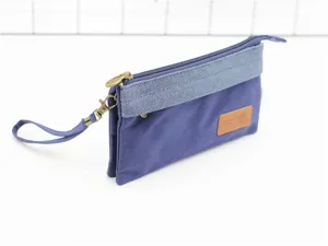 Détail de la pochette en toile unie avec lanière de poignet et fermeture éclair métallique.