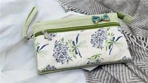 Dettaglio della borsa da polso in tessuto pastorale fresco con stampa floreale e doppia zip.