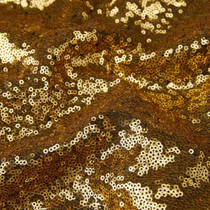 Primo piano di tessuto di paillettes dorate di lusso con una texture densa e scintillante.