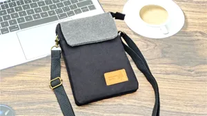 Canvas crossbody phone bag in black and gray, featuring adjustable strap and handy storage pocket.