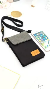 Close-up detail of black canvas crossbody phone bag with grey flap and adjustable strap.