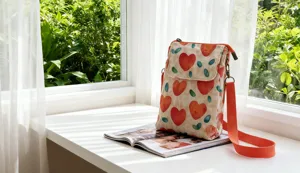 Detail view of the floral crossbody phone bag with red hearts and orange strap on windowsill.