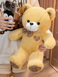 Cute yellow teddy bear plush toy detail shot showing soft fabric, bow tie, and heart patch.