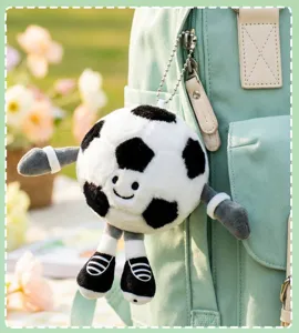 Close-up detail of a cute cartoon soccer plush keychain pendant hanging on a green backpack.