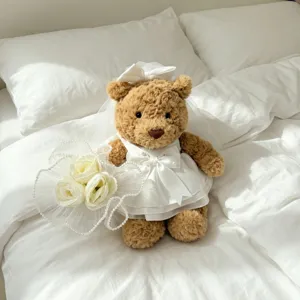Charming plush teddy bear wearing a elegant white wedding dress and veil with flower bouquet.
