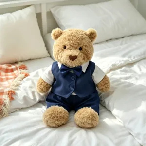 Close-up of a cute fluffy teddy bear wearing a stylish blue vest and bow tie set on a cozy bed.