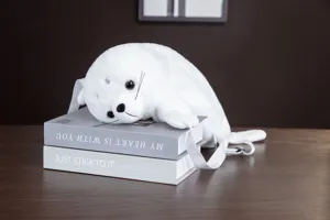 Primo piano dettagliato dell'adorabile zaino in peluche di foca bianca su libri decorativi.