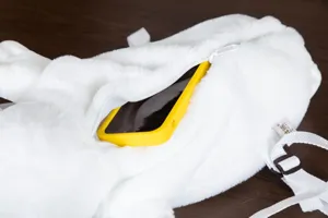 Vista dettagliata della tasca con zip dello zaino in peluche bianco a forma di foca con cellulare.