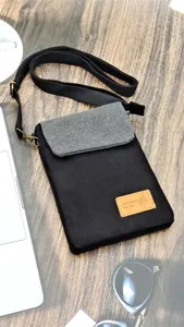 Detail view of the black and grey canvas cross-body phone bag, featuring a small handmade label.