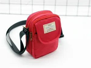 Dettaglio della mini borsa a tracolla in nylon rosso con etichetta frontale e doppia chiusura.