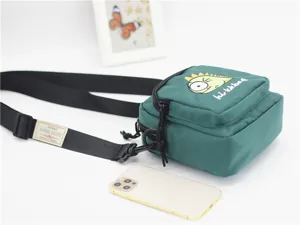 Close-up view of the green nylon crossbody bag showing cute monster embroidery and strap.