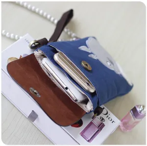 Canvas crossbody phone bag detail shot, featuring cute cartoon embroidery and brown leather flap.