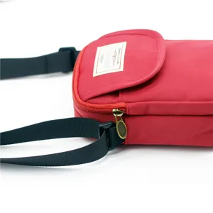 Primo piano del dettaglio della borsa a tracolla in nylon rosso, con cerniera ed etichetta.
