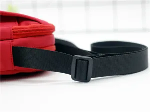 Primo piano del cinturino in nylon nero regolabile e della fibbia su una borsa a tracolla rossa.