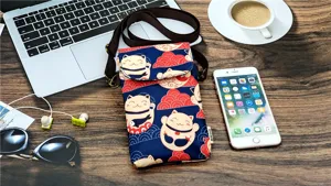 Detailed view of lucky cat pattern crossbody phone bag on wooden desk with tech accessories.