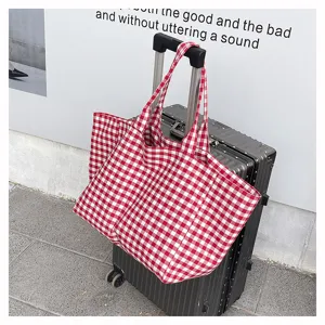 Détail du sac cabas à carreaux rouge et blanc suspendu à la poignée de la valise