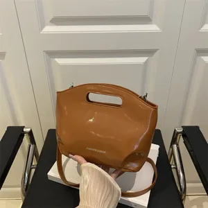 Brown patent leather underarm shoulder bag with cutout handle and detachable strap.