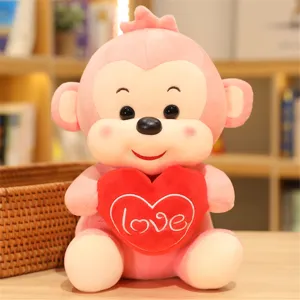 Close-up detail of a cute pink plush monkey holding a red heart pillow with love embroidery.