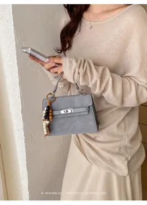 Grey top handle handbag detail, minimalist retro style lock bag with chic wooden bead charm.