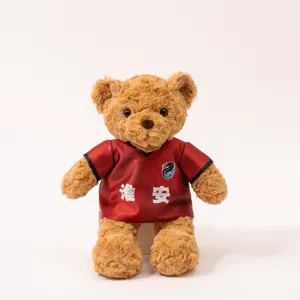 Cute brown teddy bear plush toy wearing a red football jersey with custom text and club crest detail.