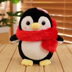 Grazioso pinguino di peluche con sciarpa rossa e fiocco, morbido tessuto in primo piano.