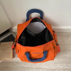 Large capacity solid color travel duffel bag detail, orange canvas weekender bag with blue handles.