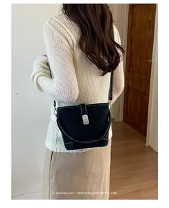 Vue détaillée d'un sac seau noir avec des coutures blanches, porté sur un beau haut.