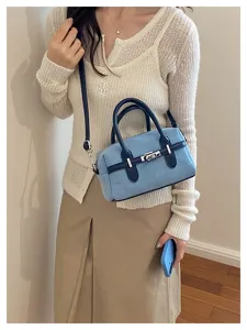 Detail shot of stylish blue denim shoulder handbag with dark blue handles and metal buckle.