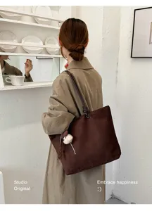 Detail view of a stylish brown tote bag with cute plush pendant, casual shoulder wear.