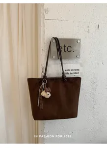 Detailed view of the dark brown tote bag hanging on a white textured wall with cute puppy pendant.
