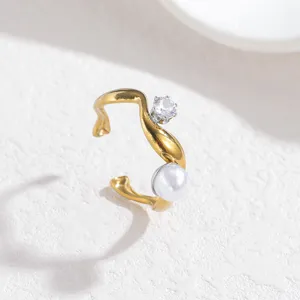 Nahaufnahme eines asymmetrischen, goldfarbenen offenen Rings mit Kristall und Perle.