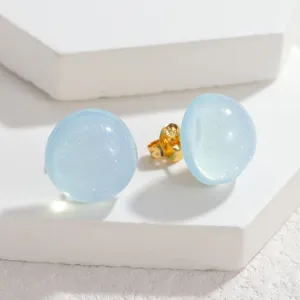 Detail view of light blue glitter dome stud earrings with gold backing on white blocks.