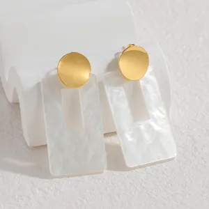 Vista de detalle cercana de los elegantes pendientes geométricos dorados y blancos.