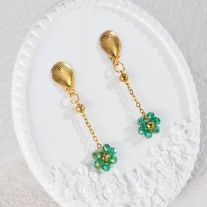Primo piano degli orecchini dorati con perline di cristallo verde e perni a forma di conchiglia.