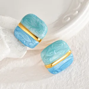 Primo piano dettagliato di orecchini quadrati marblati blu con barra dorata chic.
