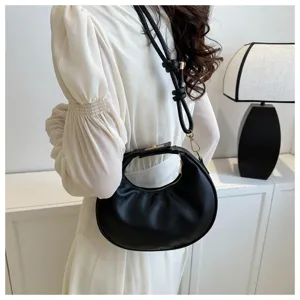 Dettaglio di una elegante borsa a mezzaluna nera indossata in un ambiente bianco minimalista.