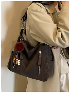 Vista detallada de un bolso hobo marrón oscuro con pompón de felpa y cremallera práctica.