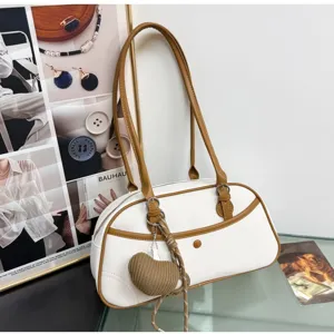 Close-up of stylish white and brown shoulder baguette bag with cute knitted heart pendant charm.