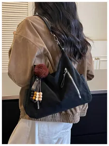 Vista detallada de un bolso de hombro negro suave con colgante de pompón y bolsillo.