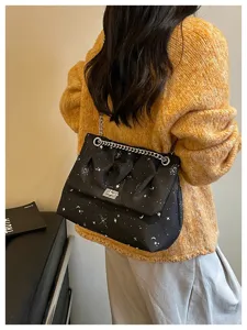 Élégant sac à épaule noir avec motif d'étoiles, chaîne et fermoir tournant chic.
