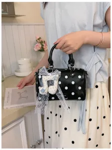 Detail view of stylish black polka dot barrel handbag with cute musical note lace pendant.