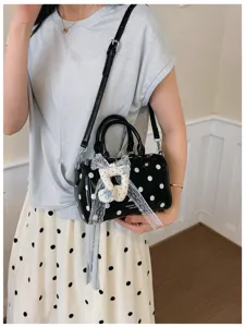 Polka dot handbag detail view, black and white shoulder bag with lace bow and cute charm.