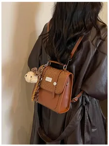 Stylish brown leather backpack for women, chic school bag with plush pendant, daily wear.