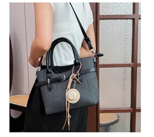 Detailed shot of a stylish dark grey women crossbody handbag with black handles and cute charm.